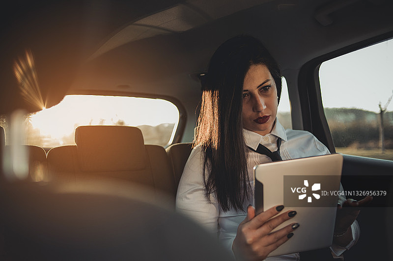 年轻黑发商务女性坐在汽车后座，在日落中前往商务会议图片素材