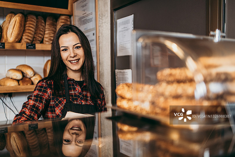 小型企业：面包店女助理快乐地递给顾客糕点图片素材