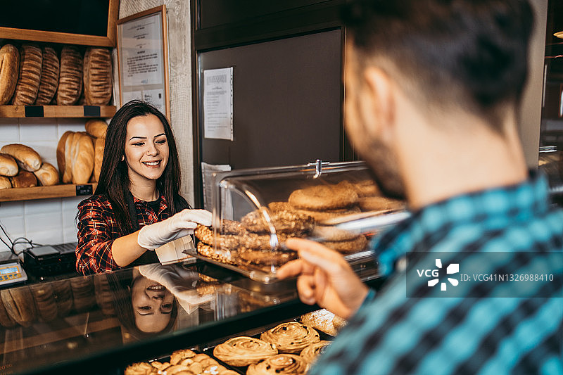 小型企业：面包店女助理快乐地递给顾客糕点图片素材