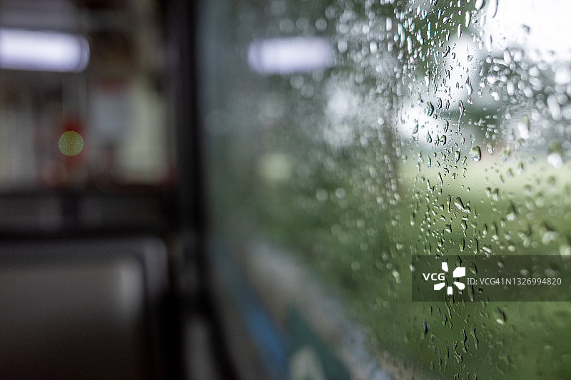 有轨电车车窗外雨滴的特写和微距视图，以及室内火车乘客的背景虚化图片素材
