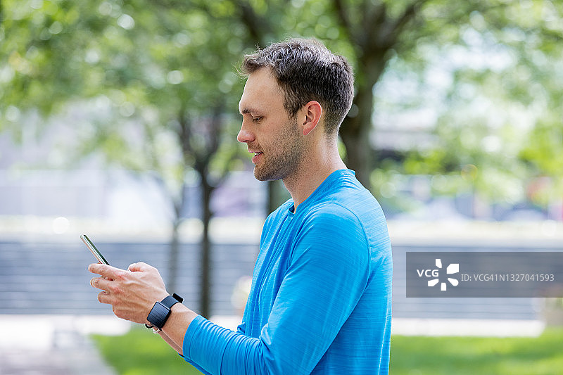 男人在城市公园慢跑时使用智能手机图片素材
