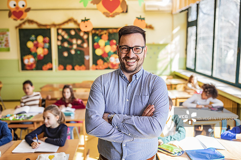快乐的小学老师在教室里交叉双臂图片素材
