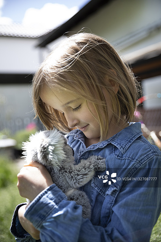 微笑的儿童(8-9岁)在春日阳光明媚的后院里抱着考拉玩具图片素材