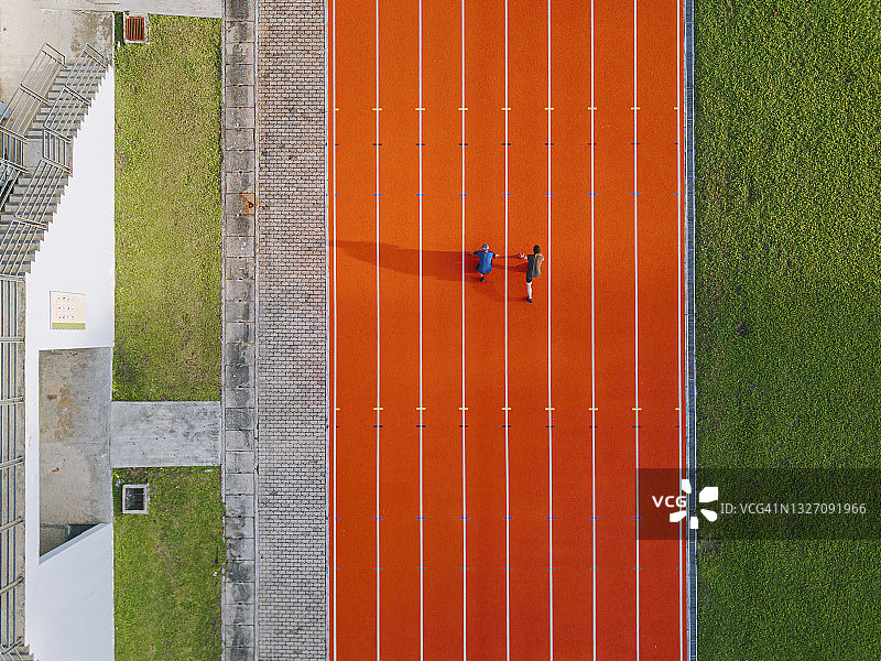 无人机俯视视角：中国父亲和儿子在跑道上准备起跑，朝着终点线奔跑图片素材