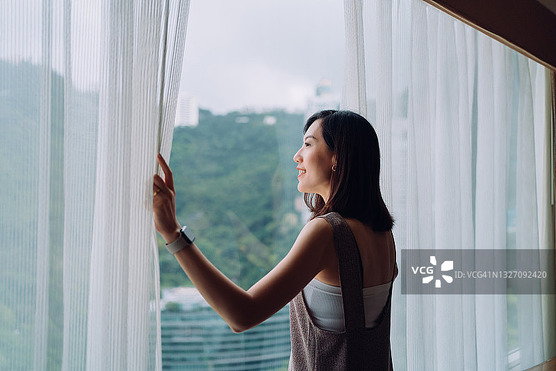 年轻亚洲女子清晨拉开窗帘欣赏美丽景色图片素材