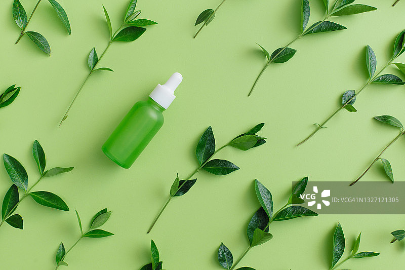 绿色玻璃瓶天然草本精华液滴管及绿叶，天然有机美容产品概念图片素材