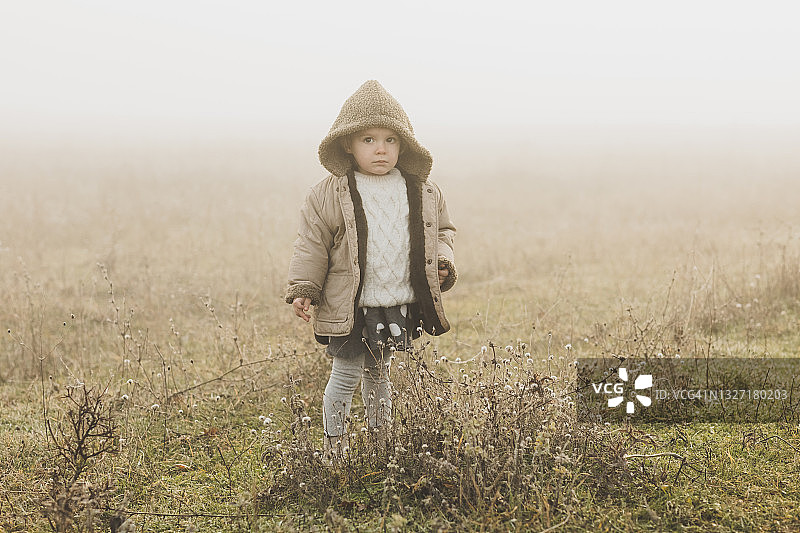 在雾蒙蒙的早晨，可爱的小女孩独自在雾中田野里图片素材