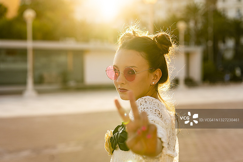少女戴着红色太阳镜在城市里展示和平手势图片素材