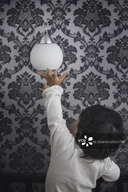 家里的女婴触摸墙上的电灯图片素材