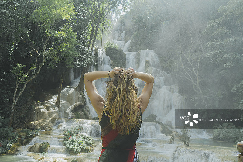 站在老挝琅勃拉邦光西瀑布前手放在头发上的年轻女人图片素材
