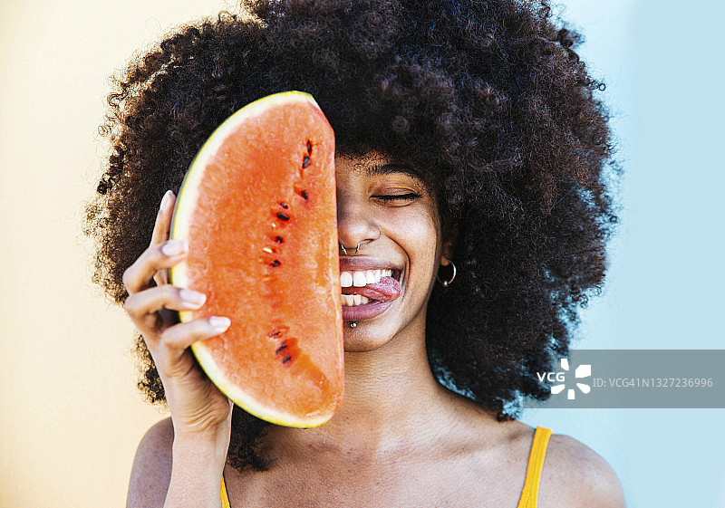 吐着舌头，在脸前拿着西瓜片的俏皮女人图片素材