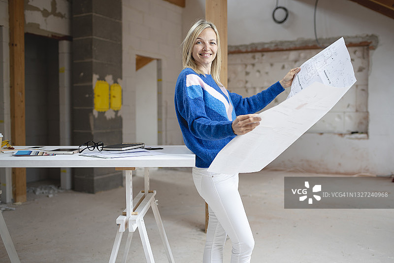 微笑的女职员在建筑工地靠在桌子上，手拿蓝图图片素材
