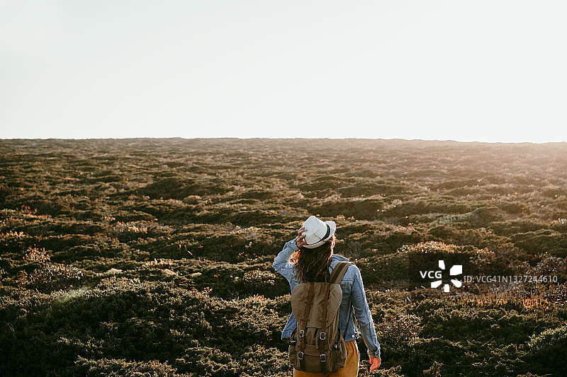 在日落时分看着草地的背着背包和戴着帽子的女人图片素材