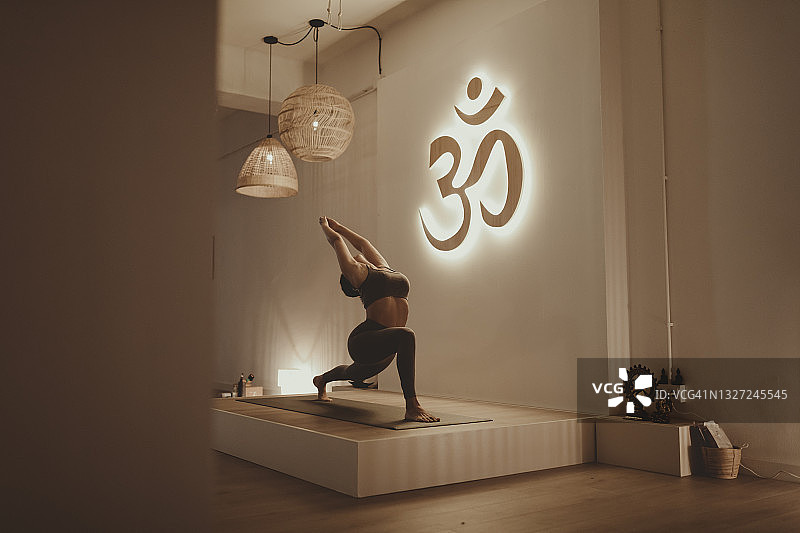 女瑜伽教练在练习时举起双臂弯腰，背景是唵字标志图片素材