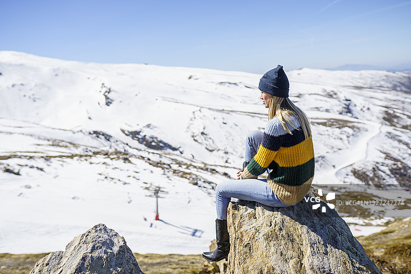 戴着针织帽坐在岩石上享受假期的年轻女人图片素材