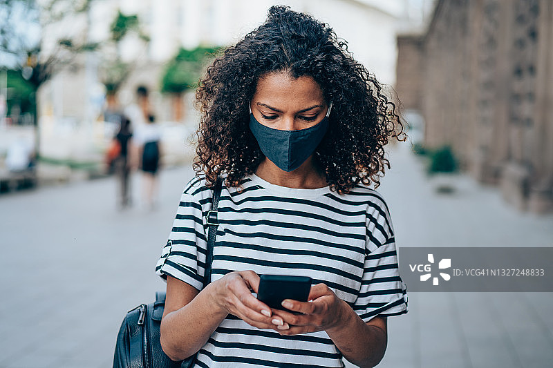 在城市户外使用智能手机的戴防护口罩的女人图片素材
