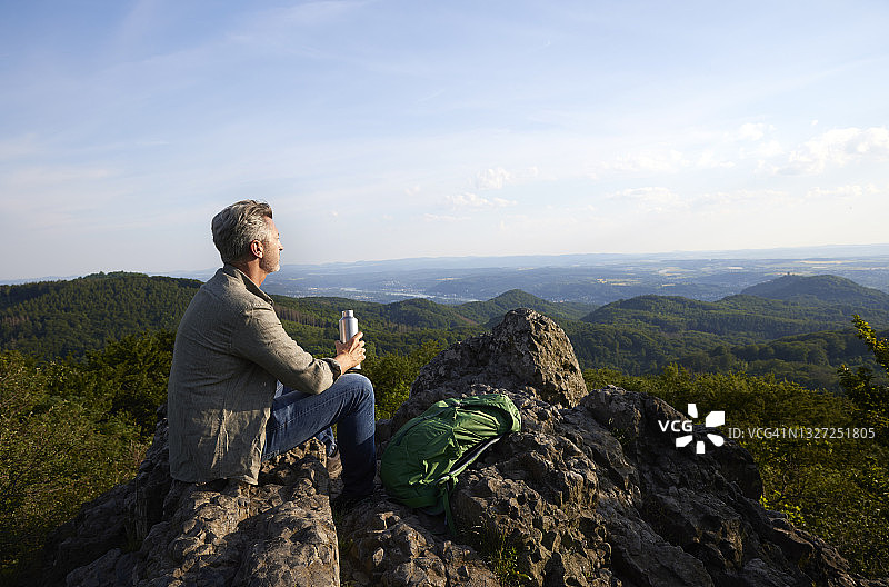 坐在山顶，手持水瓶和背包的中年男性徒步旅行者图片素材