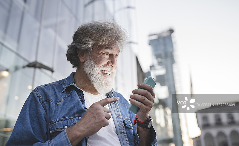 快乐的白胡子成熟男子指着大楼前的手机图片素材