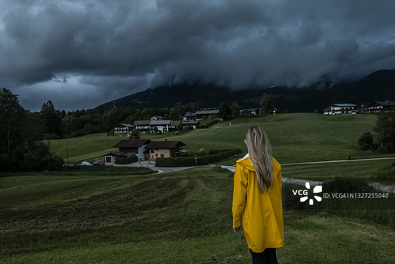 穿着黄色雨衣站在戏剧性天空下的草地上的女人图片素材