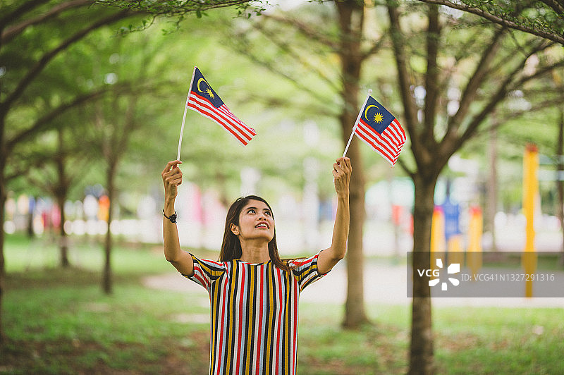 在公园里手持马来西亚国旗的美丽年轻穆斯林女性图片素材
