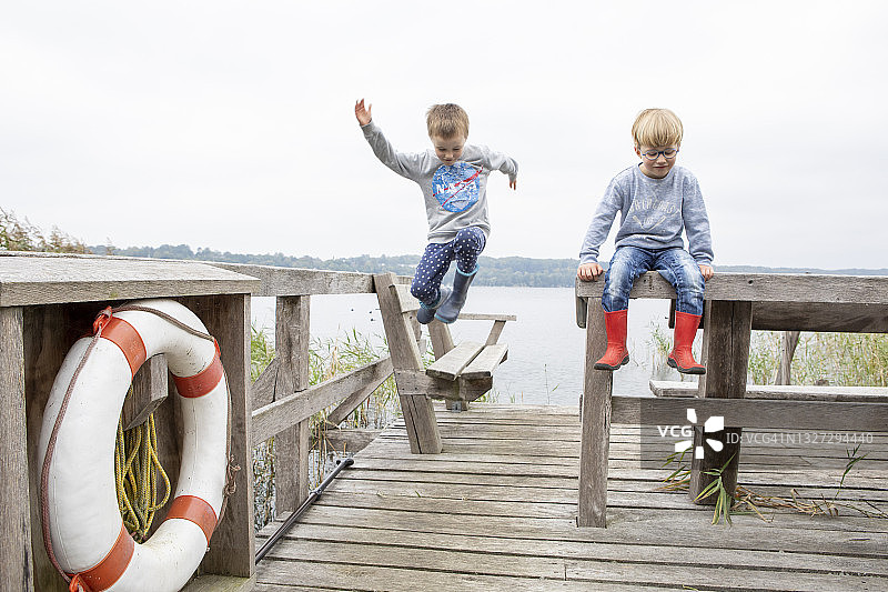 穿着雨靴的男孩在湖岸边的长椅上跳跃图片素材