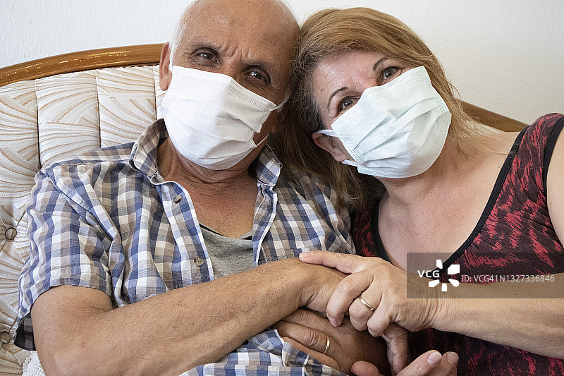 快乐的老年夫妇在疫情期间戴着口罩在家中看着镜头图片素材
