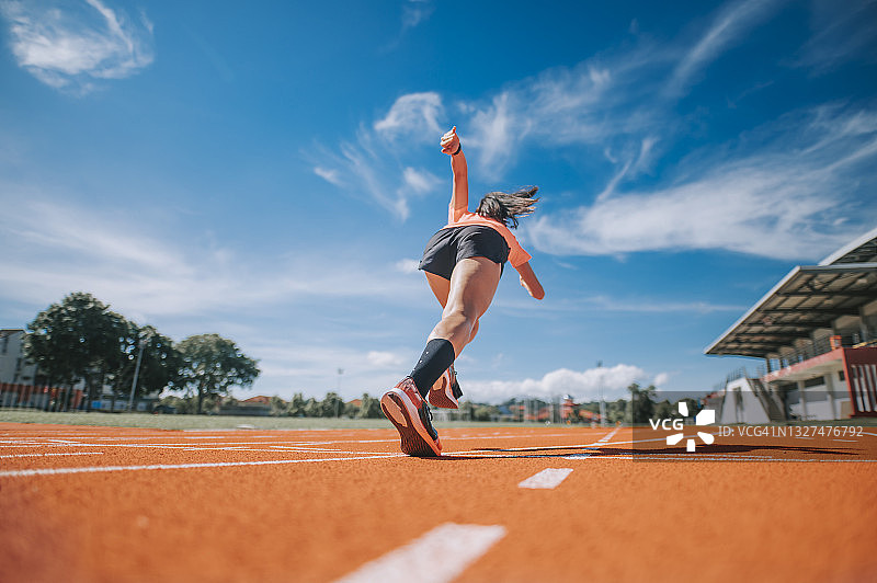 亚裔女运动员在田径场冲刺跑向终点线的后视图图片素材