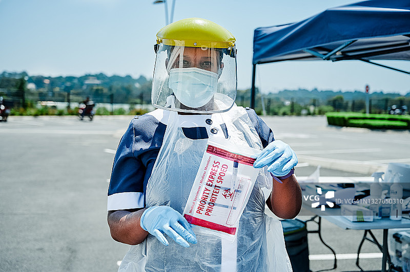 护士戴着面罩在外面拿着密封的COVID测试工具图片素材