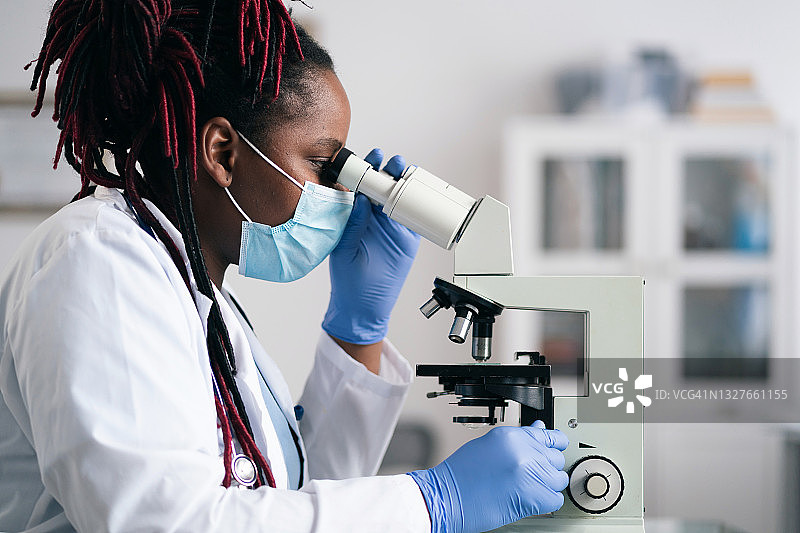 穿实验服和防护口罩的非裔美国女科学家或研究生在现代实验室工作图片素材