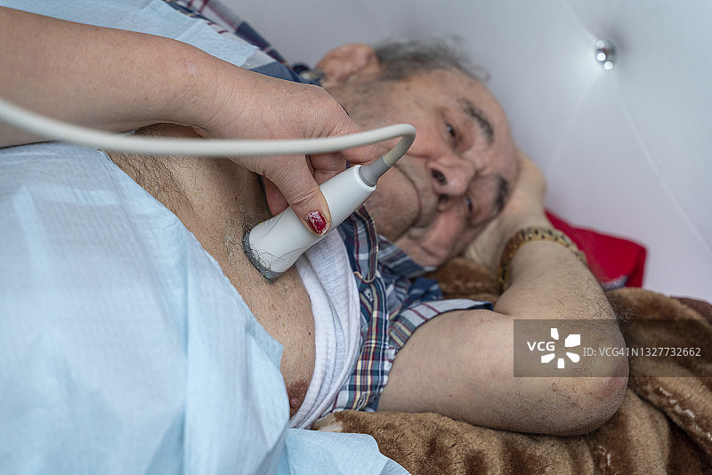 医护人员使用便携式超声设备为97岁高龄男性患者在家进行心脏超声检查，手持探头的特写镜头图片素材