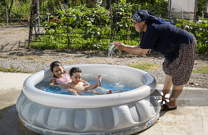 孙子孙女和奶奶在后院的充气游泳池里玩耍图片素材