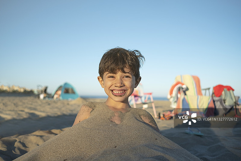 快乐的孩子被家人埋在沙滩上，看着镜头微笑图片素材