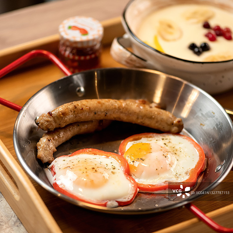 厨房桌子上平底锅里的两个煎蛋和香肠。木制托盘上的健康早餐特写镜头。柔焦图片素材