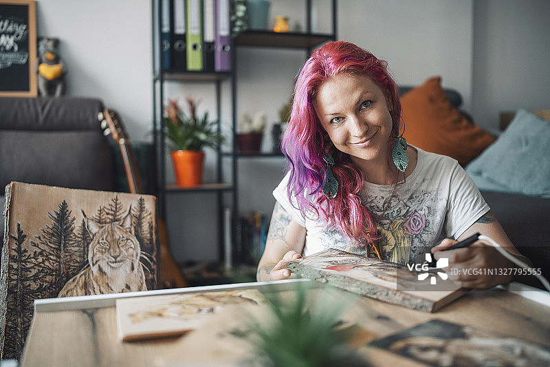 微笑的图形艺术家在木板上用热蚀画绘画时看着镜头的肖像图片素材