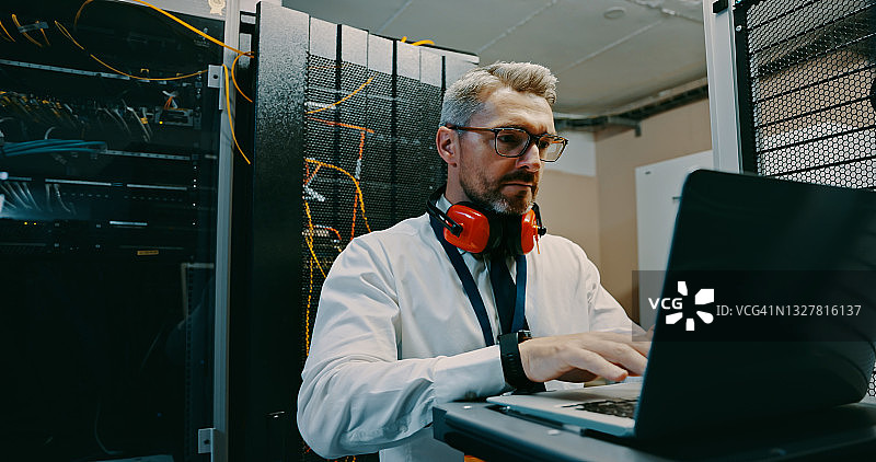 男技术员在服务器机房使用笔记本电脑工作图片素材