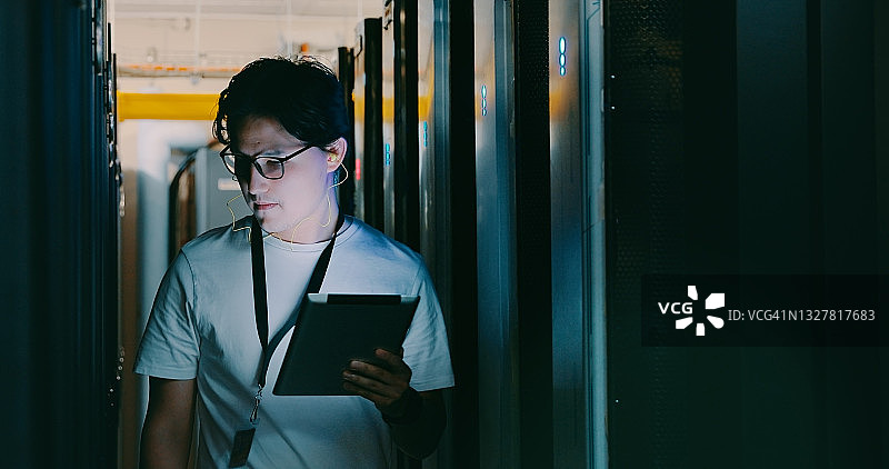 年轻男人使用平板电脑走过服务器机房的照片图片素材