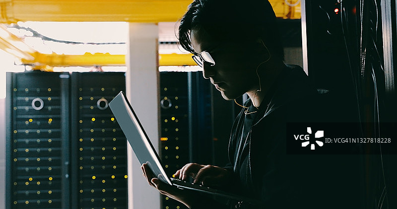 年轻黑客在服务器机房使用笔记本电脑图片素材