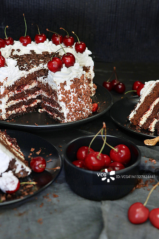 切片的黑森林蛋糕图像，裱花奶油花饰和黑樱桃，奢华巧克力蛋糕，表面覆盖巧克力碎屑，黑色盘子，黑色背景，前景聚焦图片素材