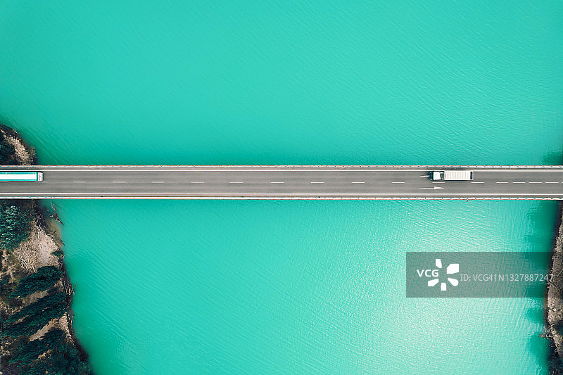 无人机视角：俯瞰大型卡车行驶在比利牛斯山脉的蓝色湖泊桥上图片素材