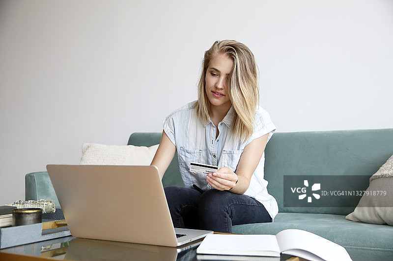 一位金发白人千禧一代女性，在居家环境中穿着休闲服装，在笔记本电脑上用信用卡付款图片素材