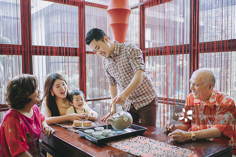 中国父亲在下午茶聚会上为家人斟茶，共度中秋佳节，品尝月饼图片素材