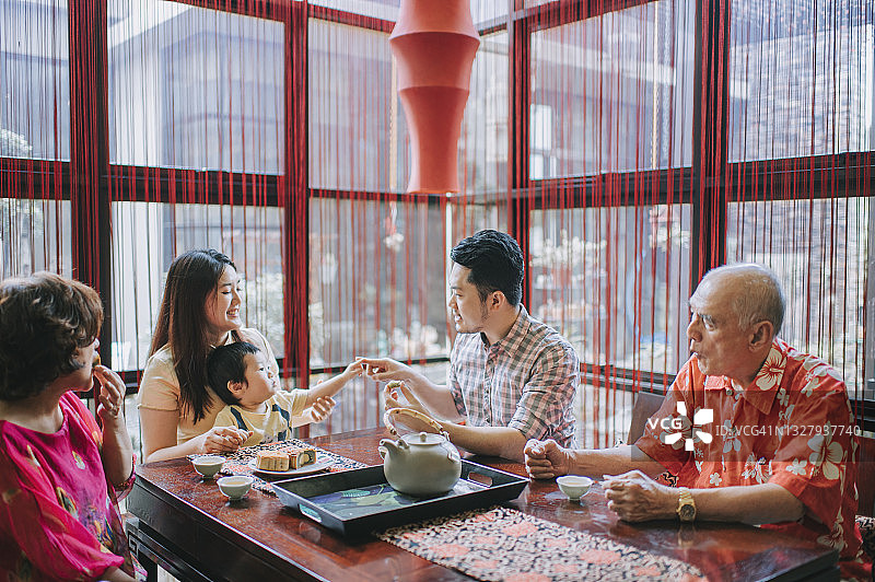 中国父亲与儿子在下午茶聚会时一同享用传统中秋月饼和中国茶图片素材