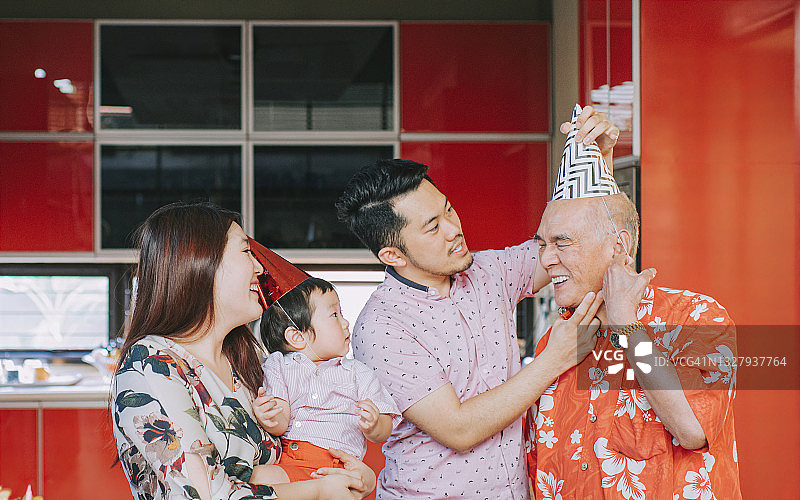 中国儿子在家中家庭庆生派对前帮助戴派对帽的父亲图片素材