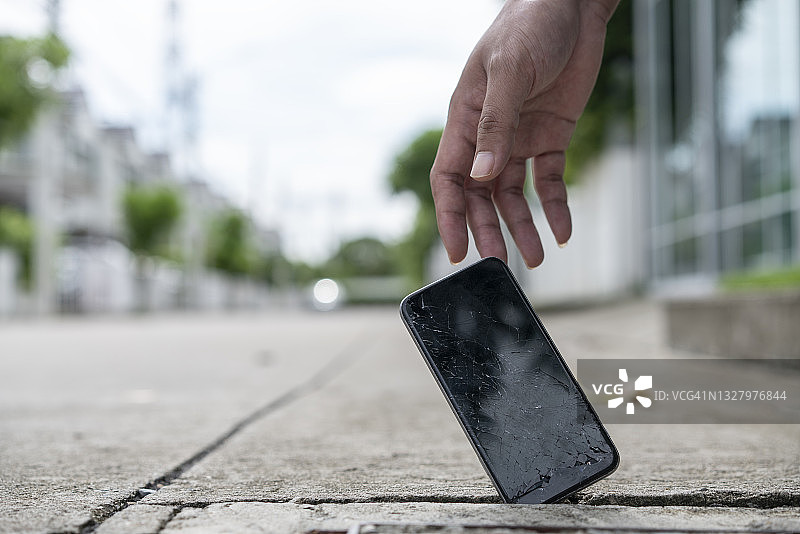 男人伸手去拿屏幕破裂的智能手机图片素材