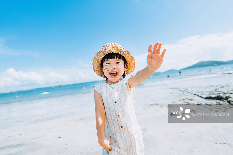 快乐的亚洲小女孩戴着草帽在阳光明媚的夏日海滩上玩耍图片素材