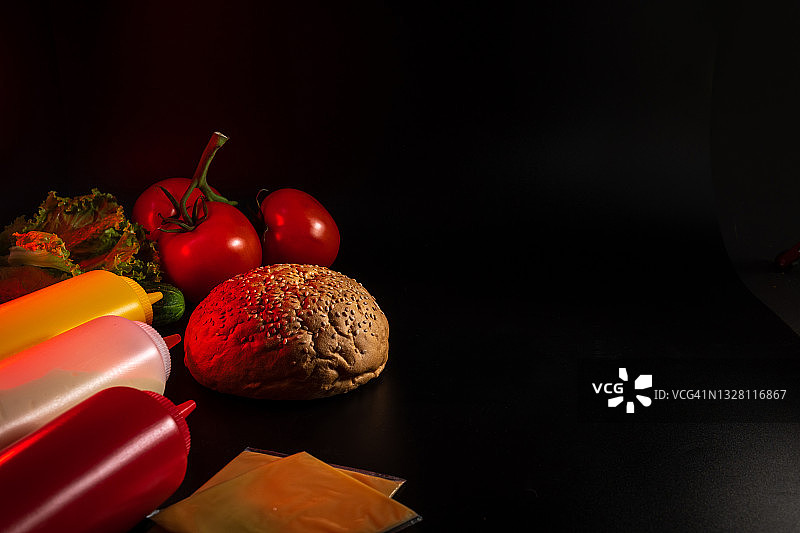 面包、汉堡面包和汉堡配料：酱汁、奶酪、沙拉和蔬菜。快餐面包生产概念，黑色背景，留白。图片素材