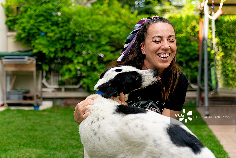 在公园草地上和她的狗玩耍的快乐年轻女人图片素材