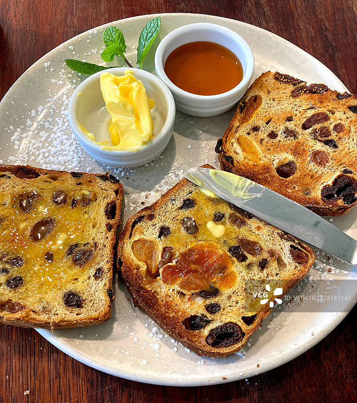 水果吐司，黄油和蜂蜜配刀放在白色盘子上图片素材