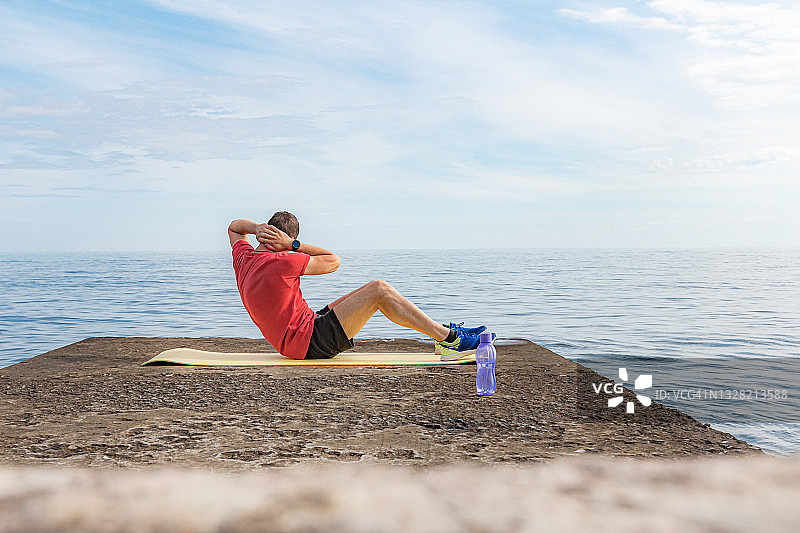 穿着红色T恤的男人在码头的运动垫上做仰卧起坐图片素材
