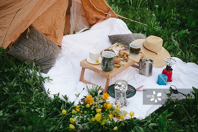 夏季野餐概念：黄色野花、白色野餐毯、茶具和绿草背景图片素材